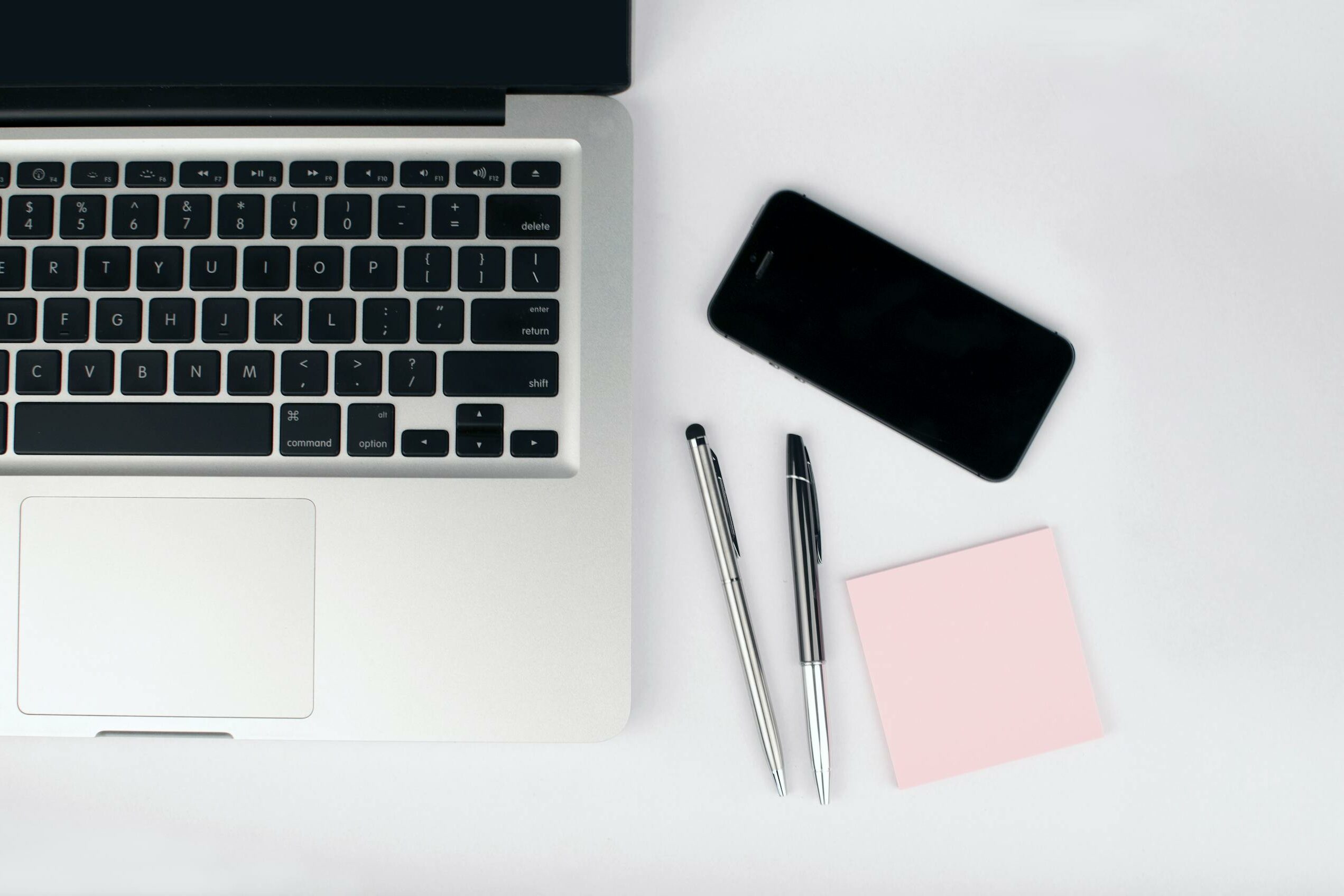 Overhead view of a sleek workspace featuring a laptop, smartphone, and stationeries on a white desk.